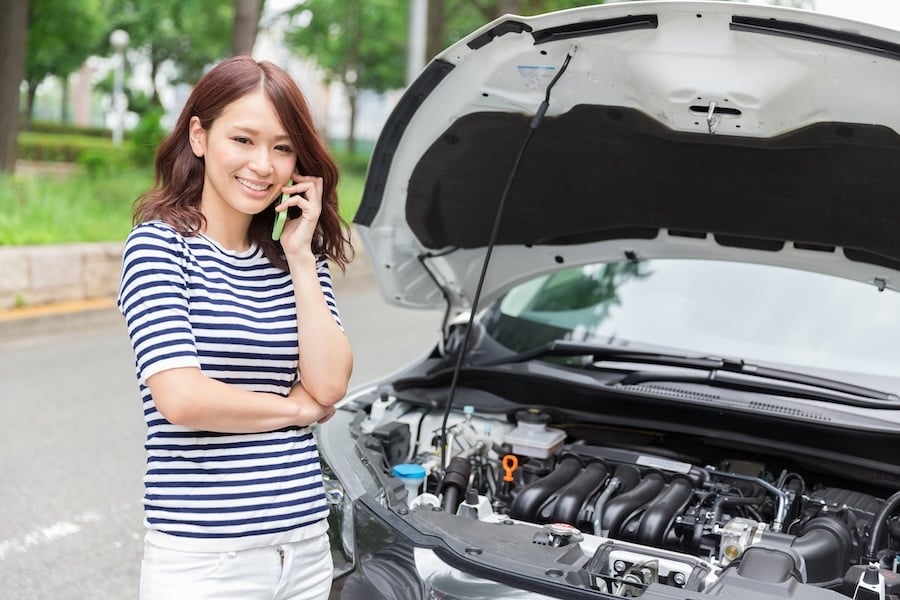 A smiling woman on the phone in front of her open car hood